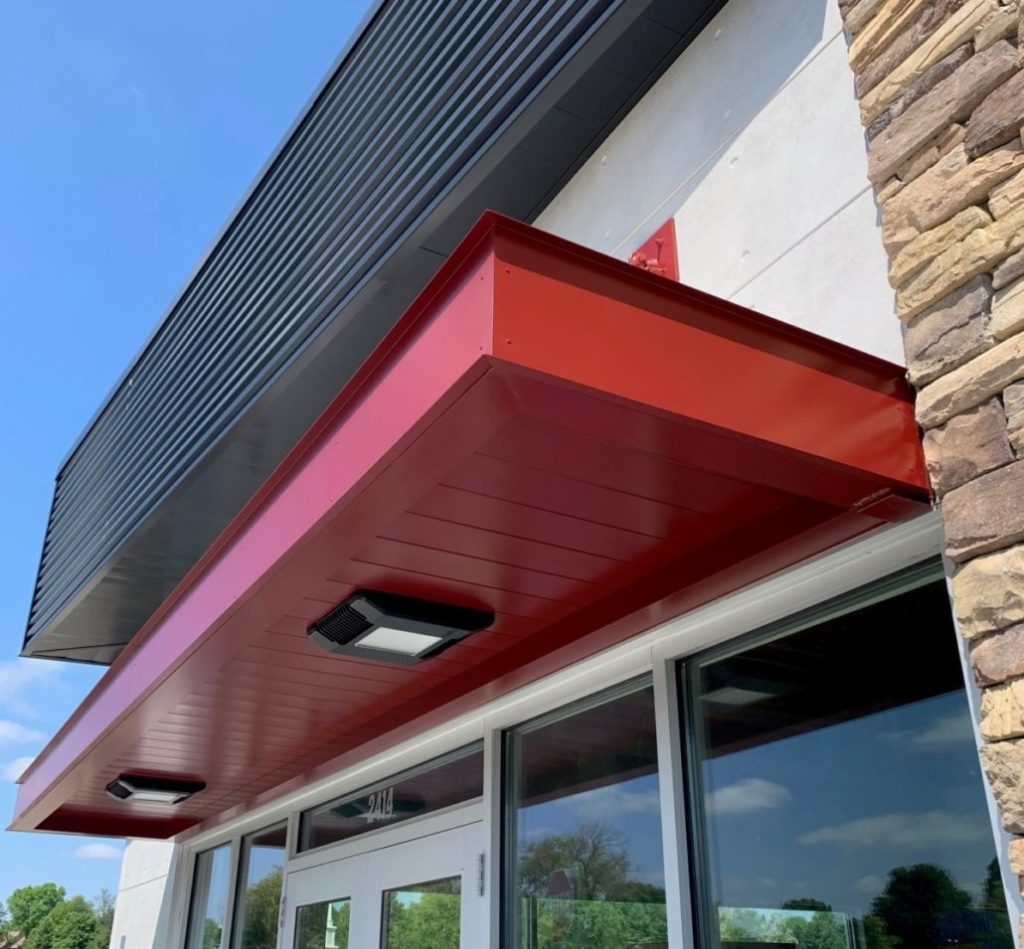 Red canopy extending over glass doors, with visible lighting fixtures and a textured stone wall.