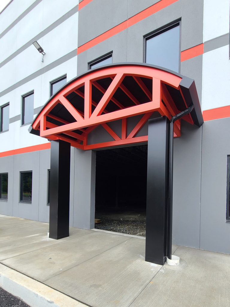 Red arched entrance with black pillars at the entrance of a modern building featuring gray and orange walls.