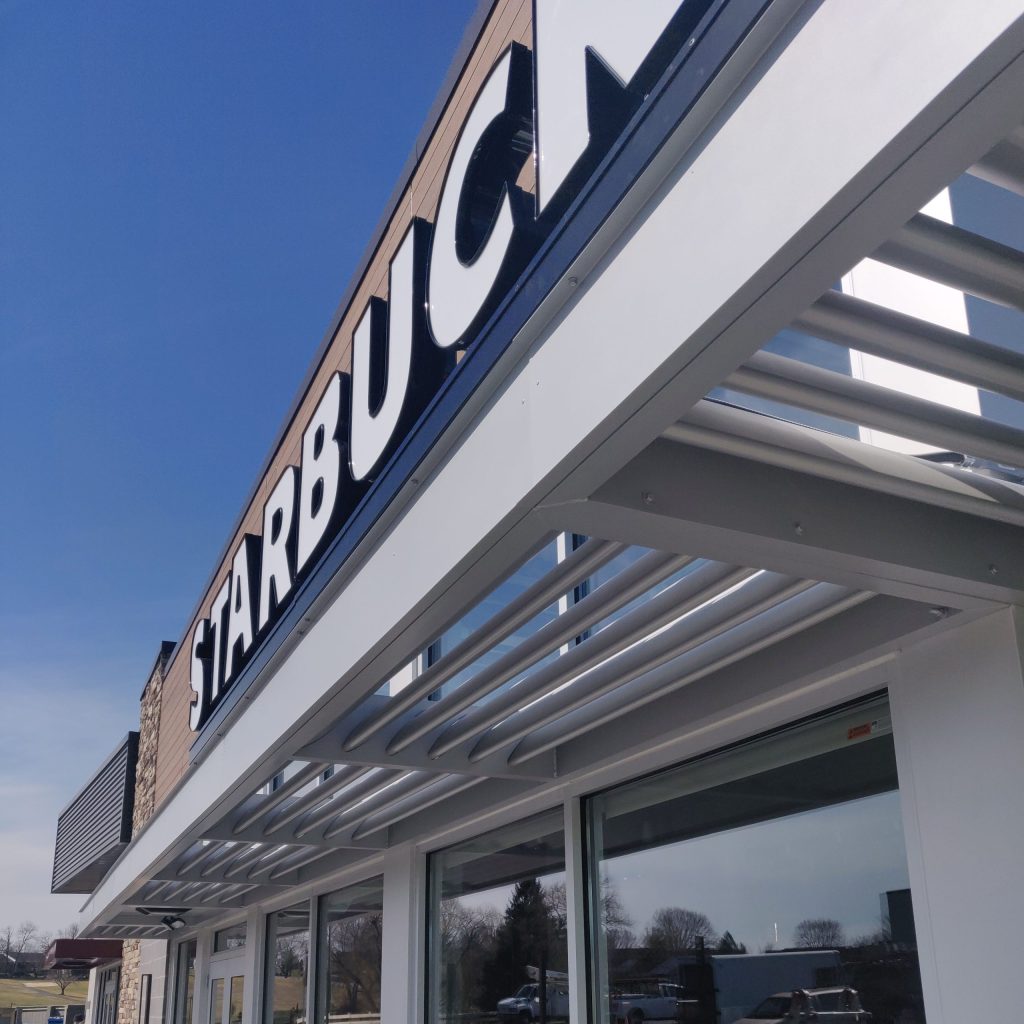 Starbucks storefront with large signage and a clear blue sky in the background.